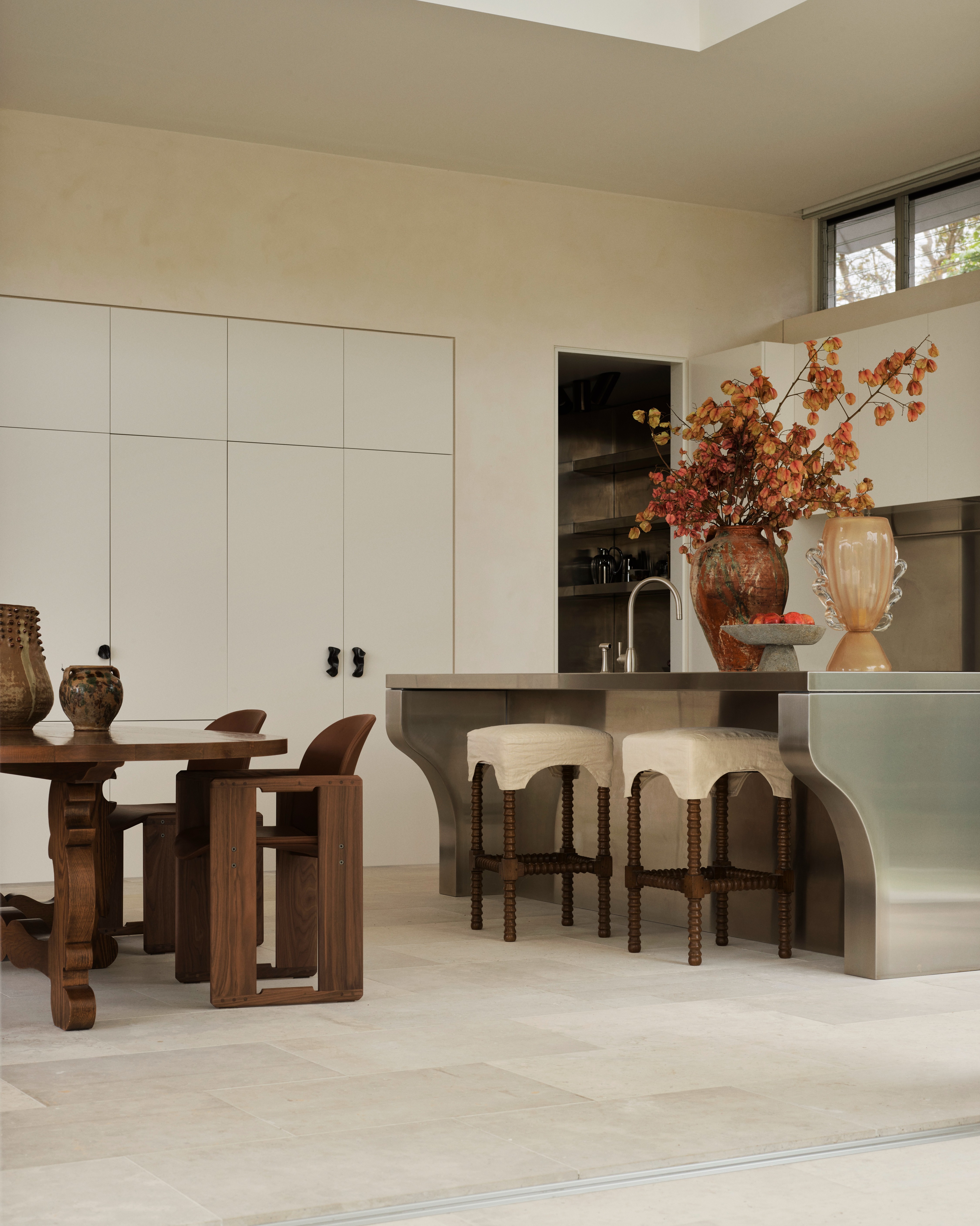 Pale plaster kitchen with stainless island, timber dining table and autumnal florals